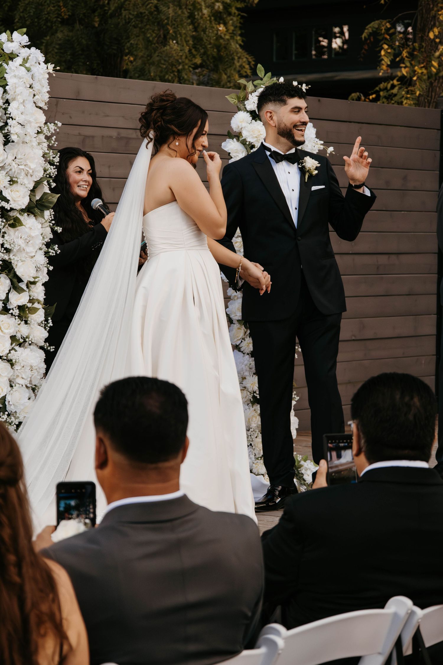 Bride and groom celebrate at outdoor wedding ceremony altar adorned with white floral arrangements.