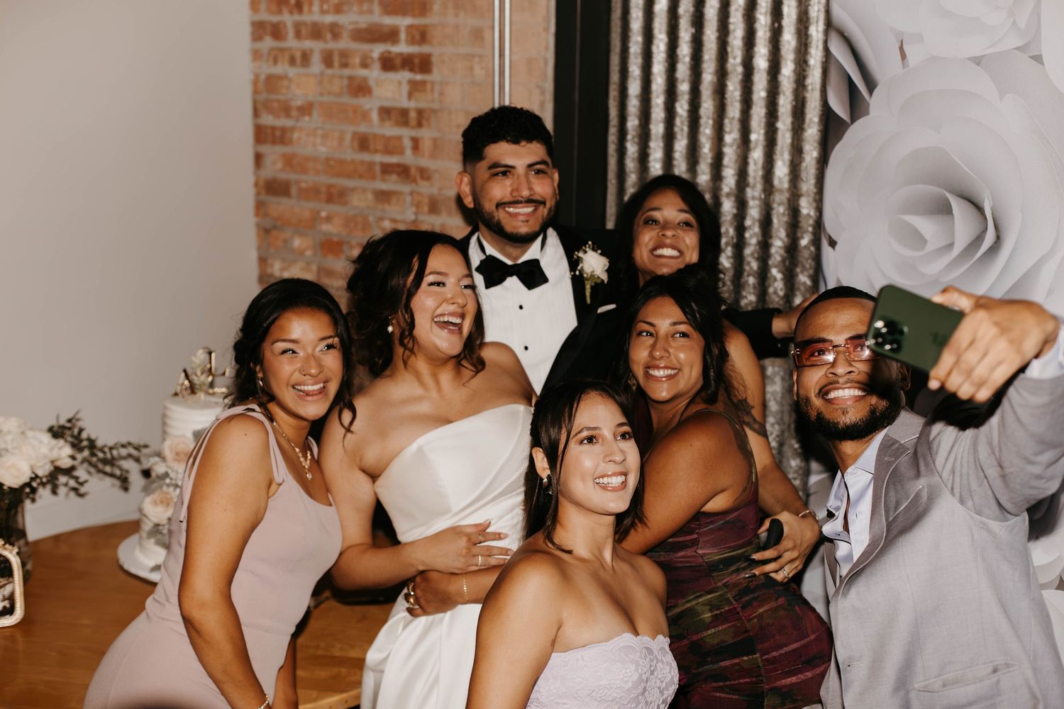 Bride and groom pose for fun selfie with wedding guests in elegant reception venue.