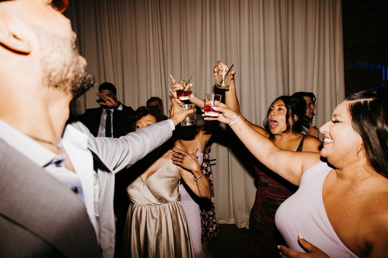 Wedding guests raise glasses in joyful toast during lively evening reception celebration.