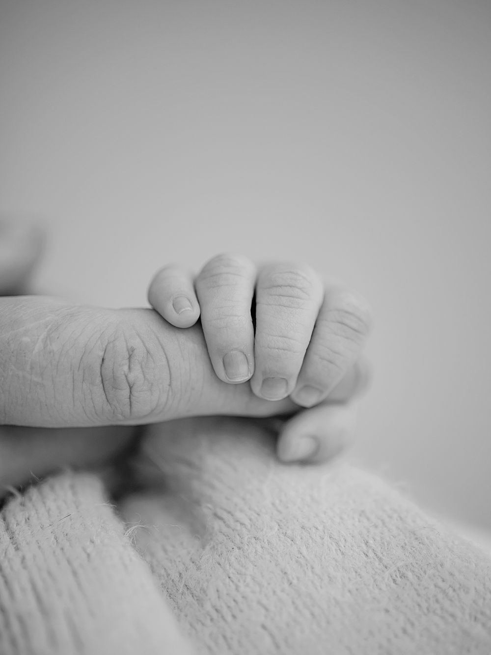 detaljbild på bebishand som håller i förälder nyfödd bebis i svartvitt, nyföddfotografering i Västerås, memoriesbym.se