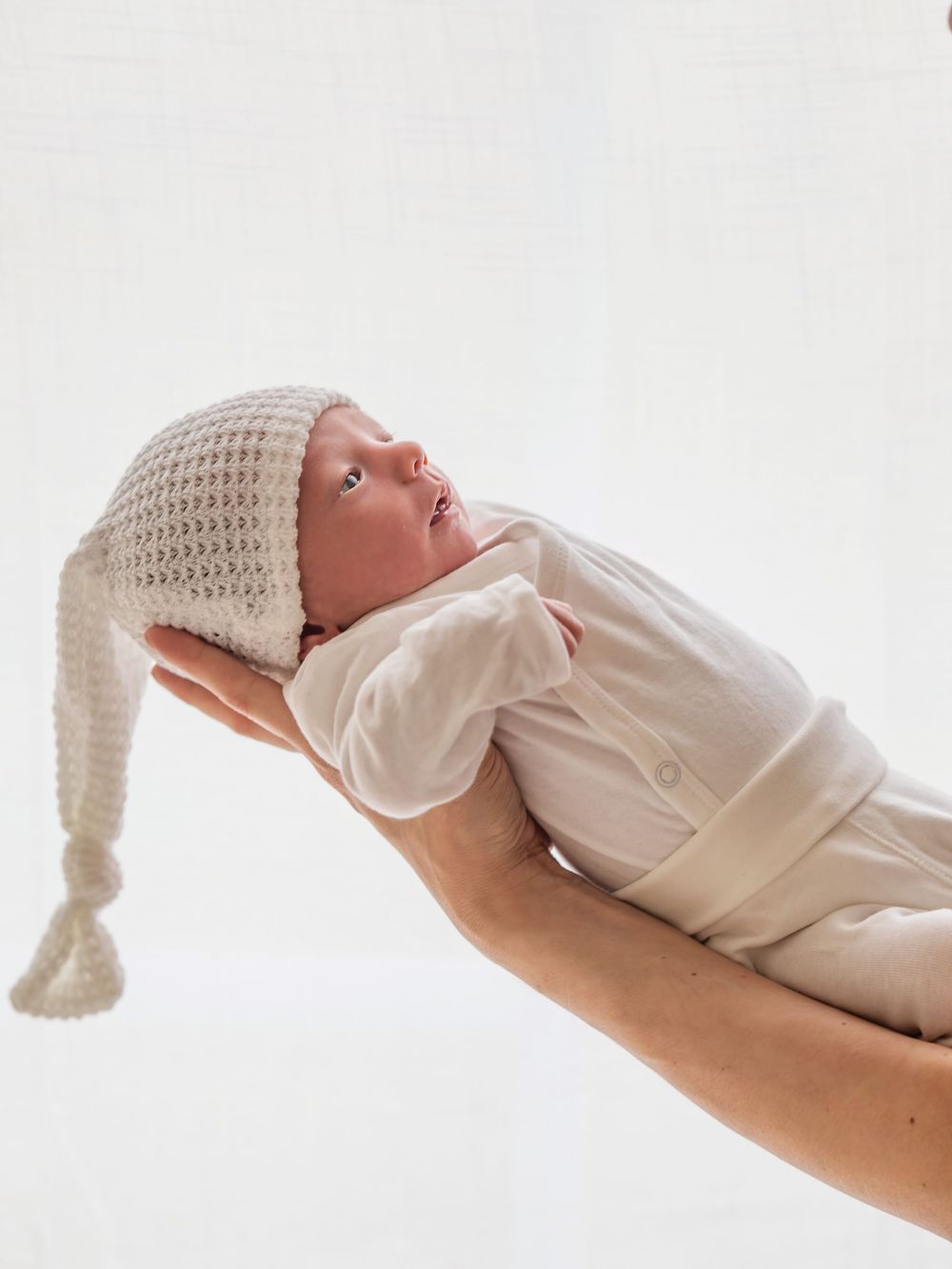 Nyfödd bebis i vit outfit, liggande i handen, nyföddfotografering Västerås, MemoriesbyM