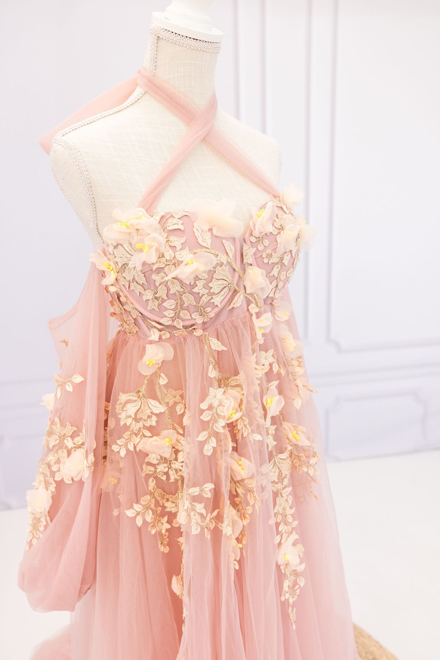 Delicate pink tulle dress with floral appliques hanging on display.