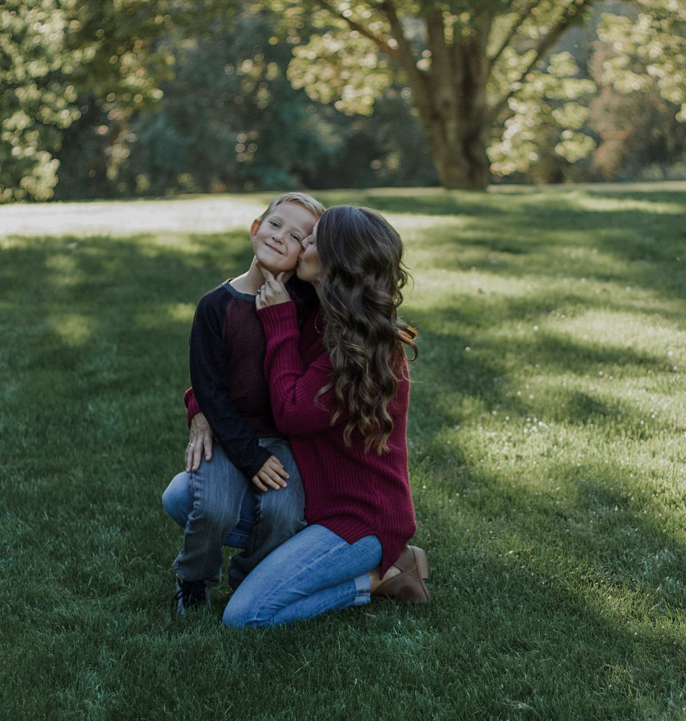 Mother and young son sharing a sweet kiss on a lush green lawn.