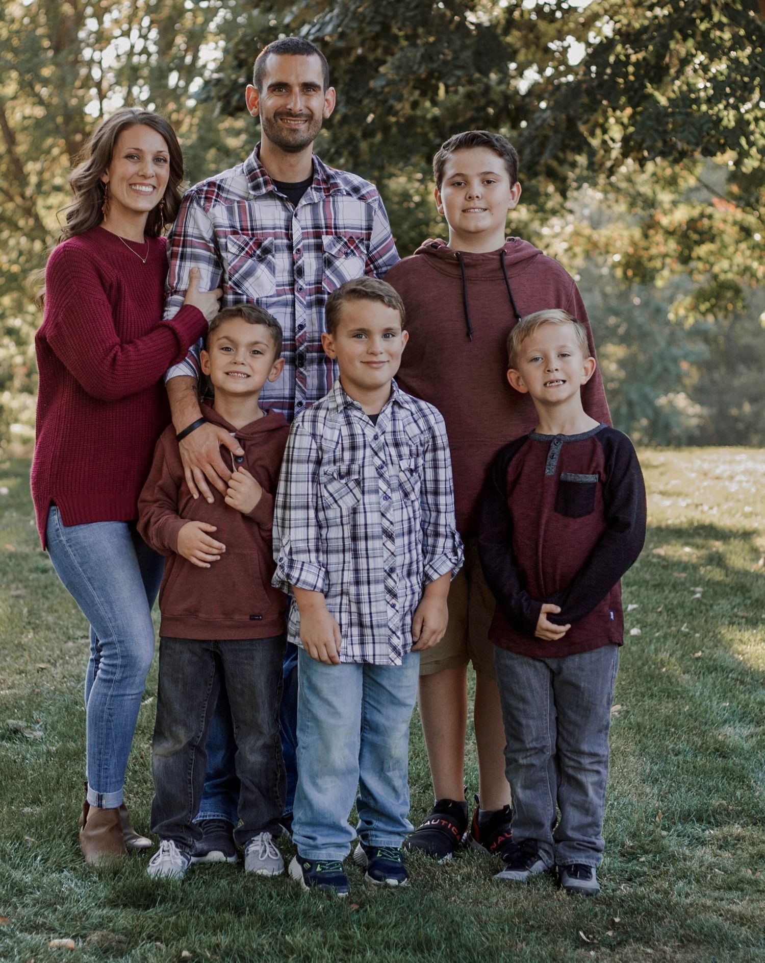 Family of six in coordinating burgundy outfits posing together in an autumn park.