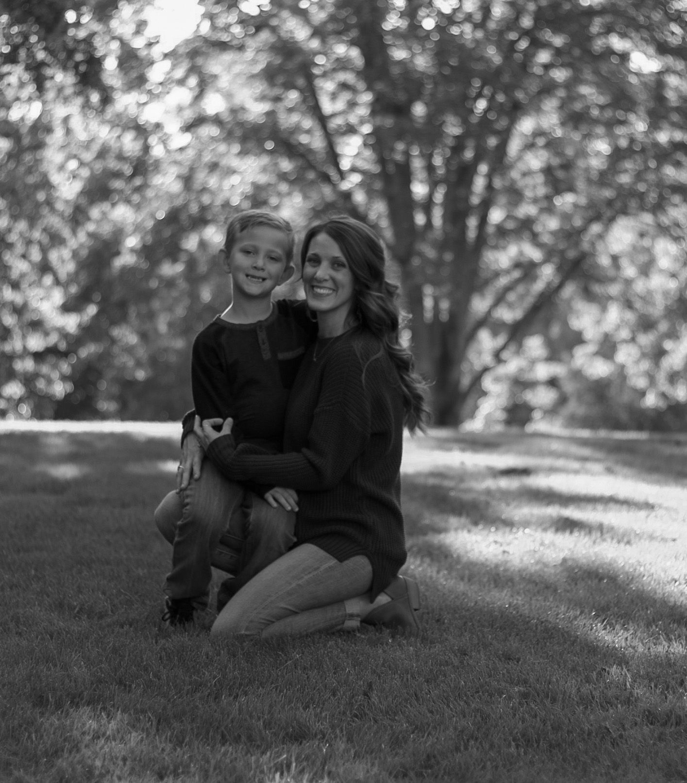 Black and white photo of a mother and young child smiling in a park.