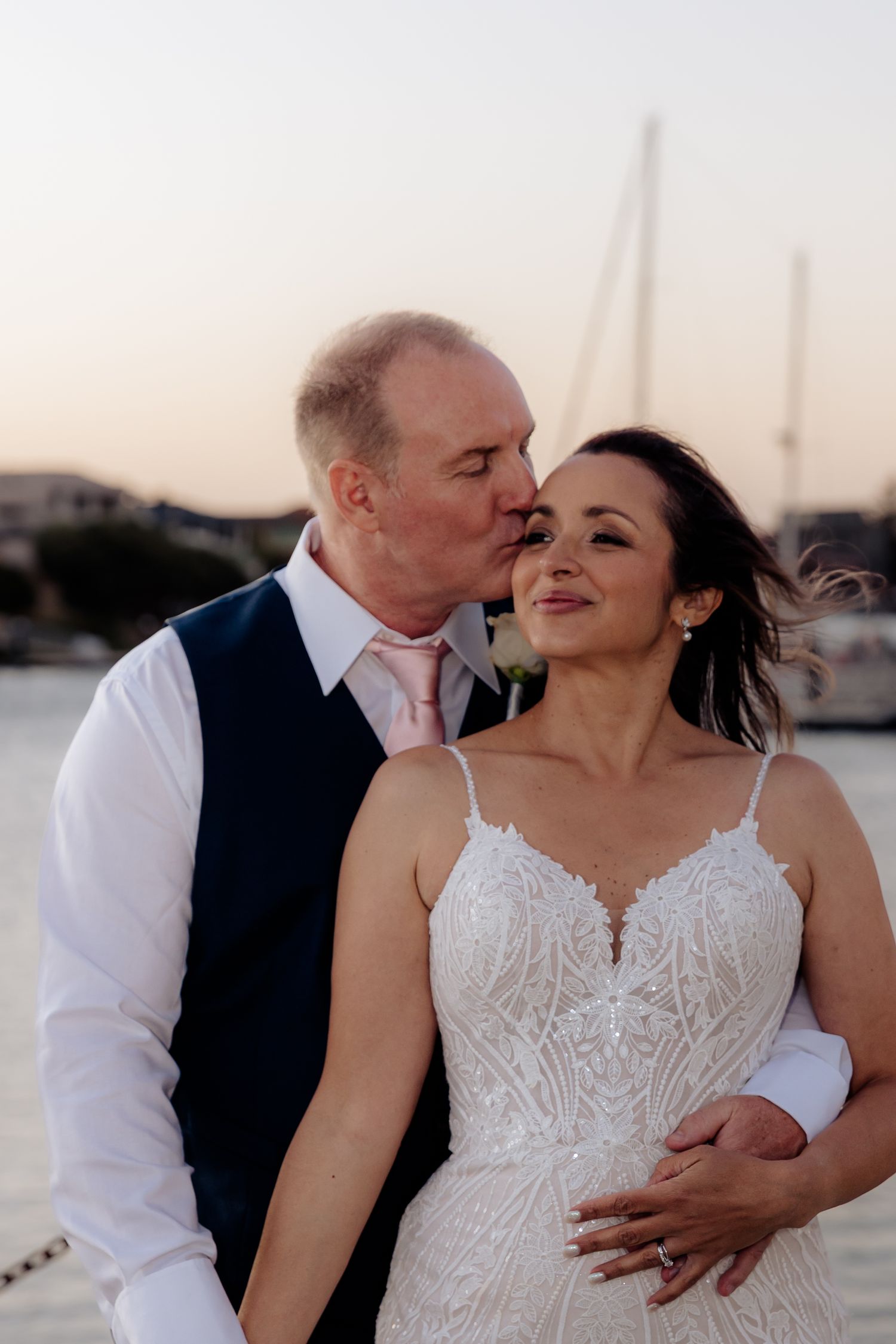 Romantic wedding couple sharing an intimate moment at sunset by the marina with boats in background.