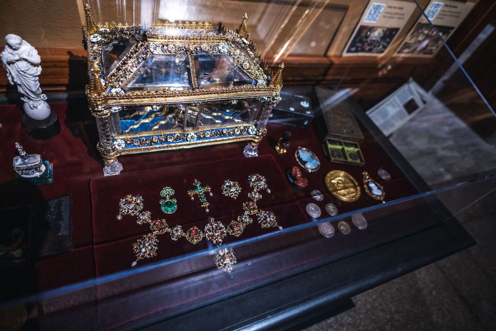Top view of a glass display case showing jewelry and ornate items arranged on a burgundy velvet surface in an antique shop.