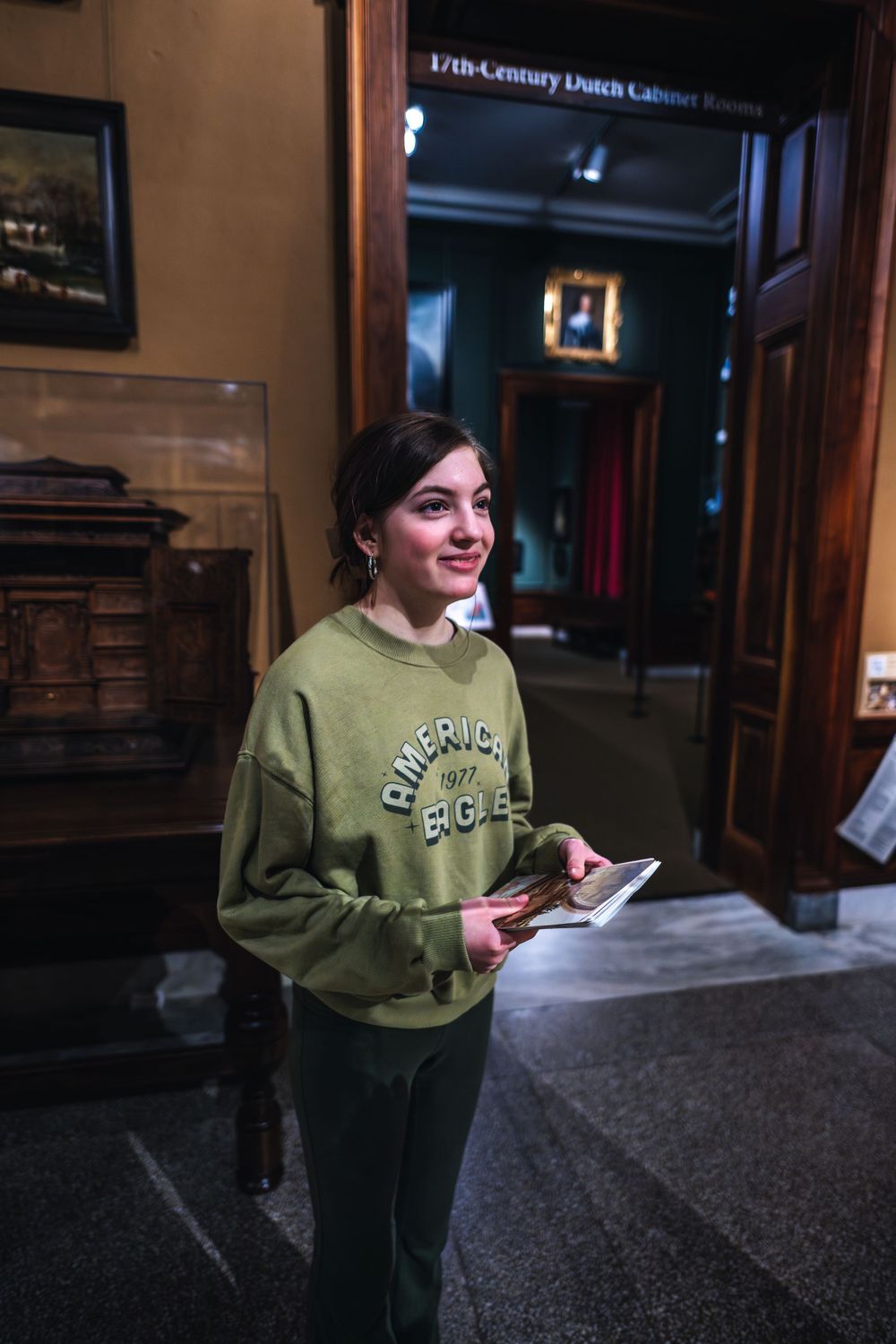Person in olive green sweatshirt holding paper while standing in a historic building hallway.