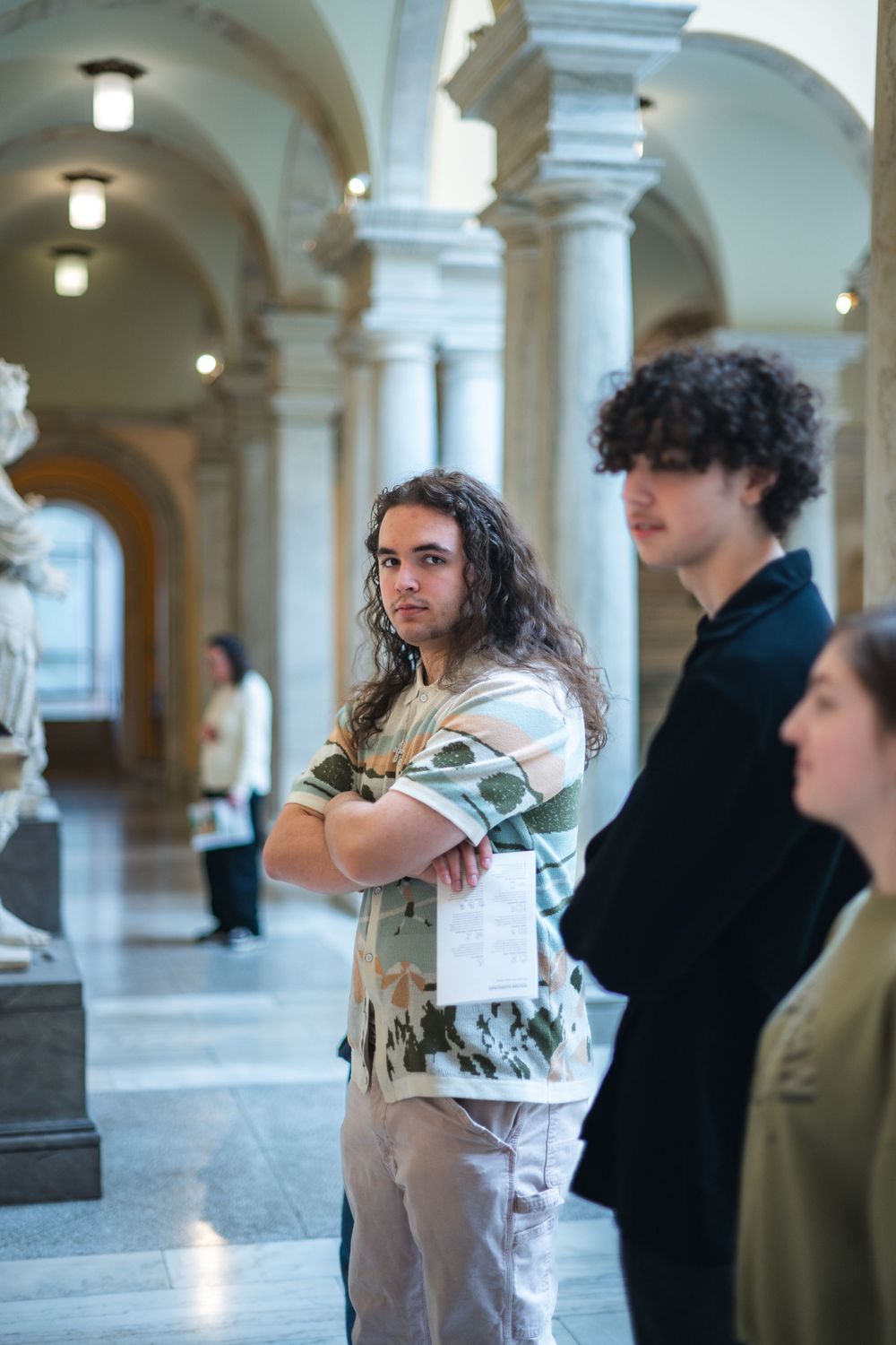 Visitors stand in an ornate museum hallway with arched columns and classical architecture illuminated by overhead lights.