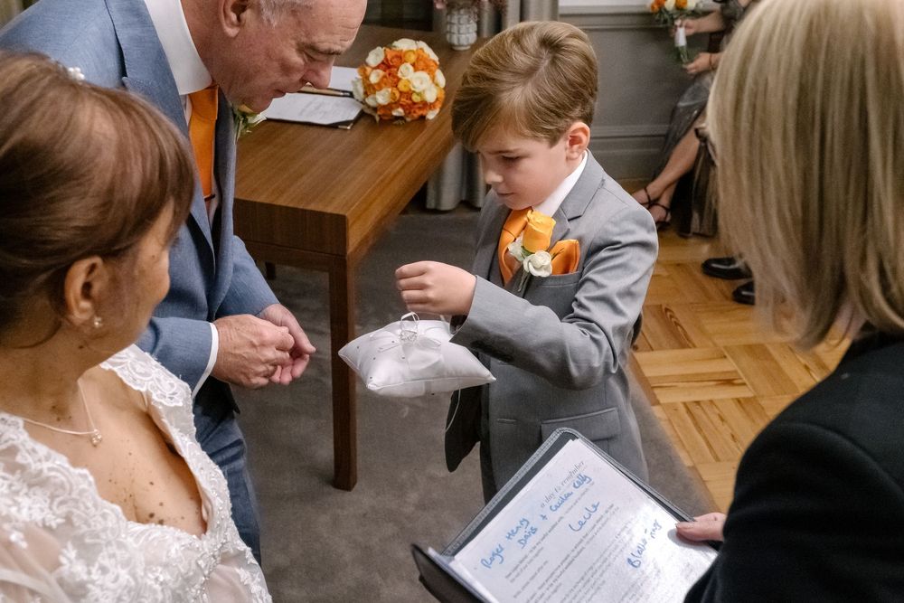 A young wedding guest follows along with a ceremony program while seated at a wooden table during an indoor celebration.