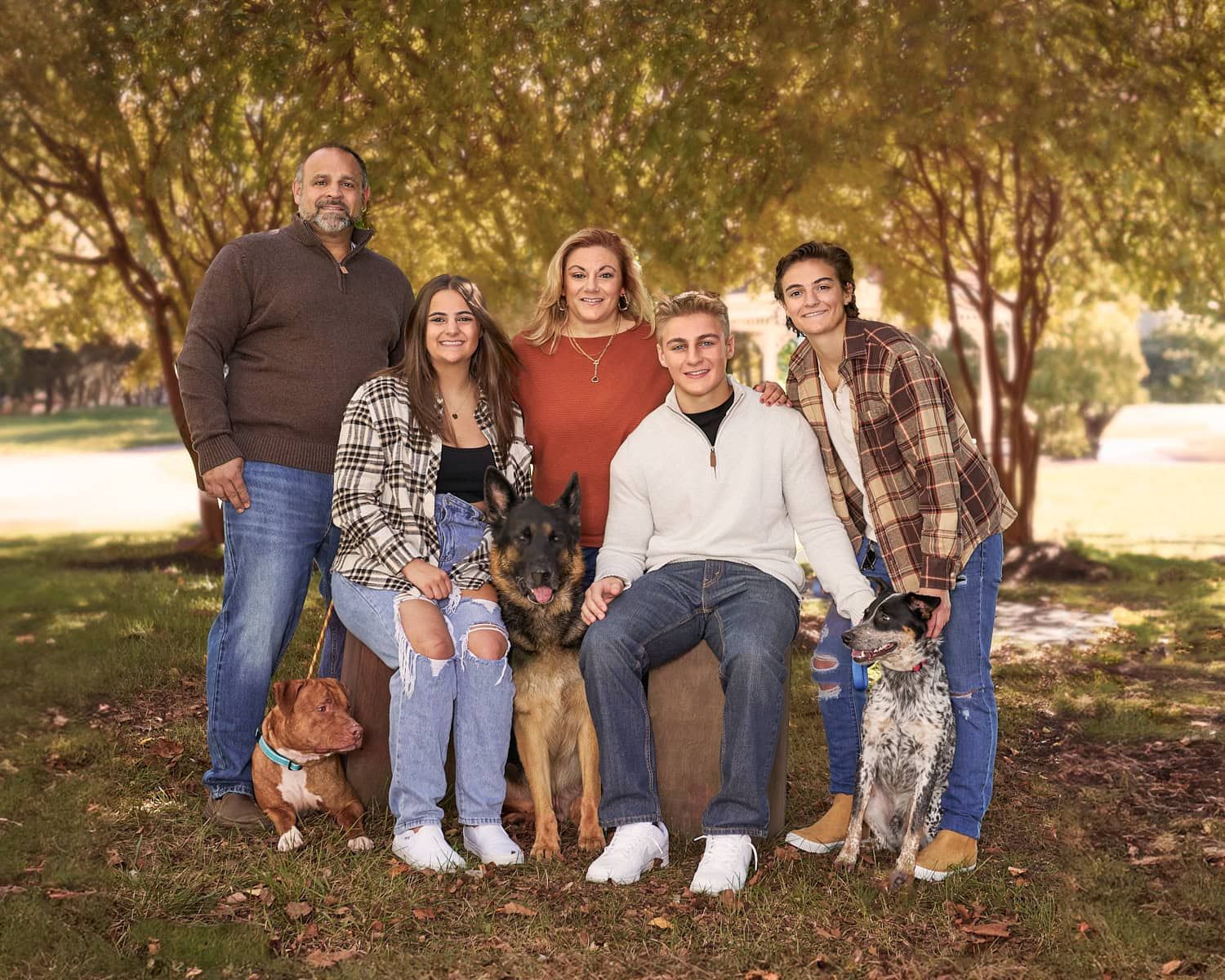Family of parents and three older teens with their three dogs in a Fall scene in front of trees