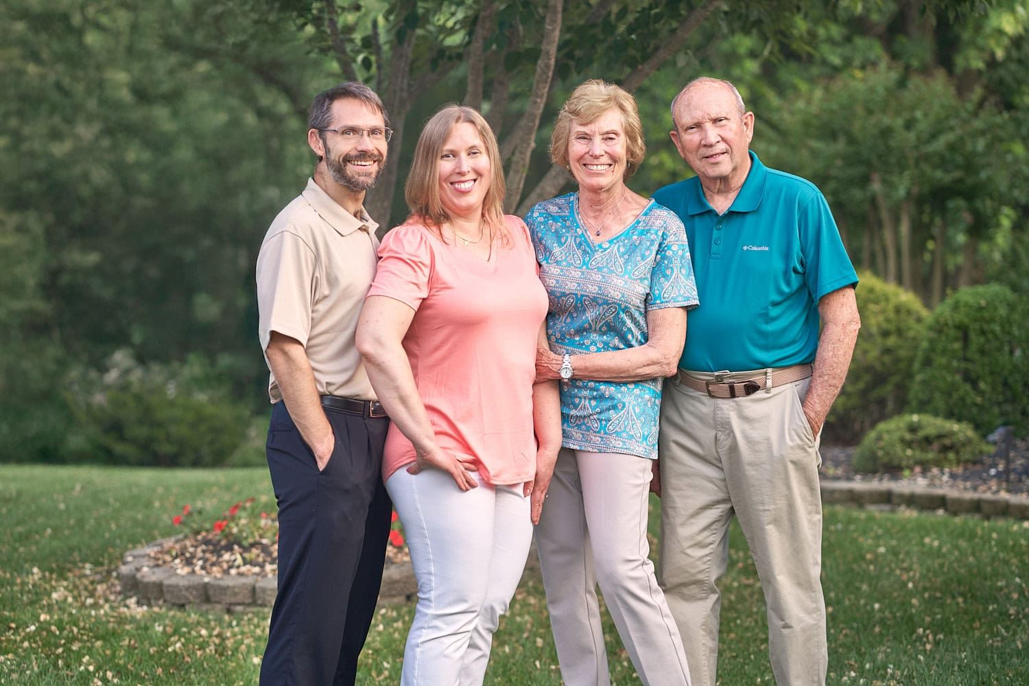 Older parents with 30-something daughter and son-in-law standing in front yard of home