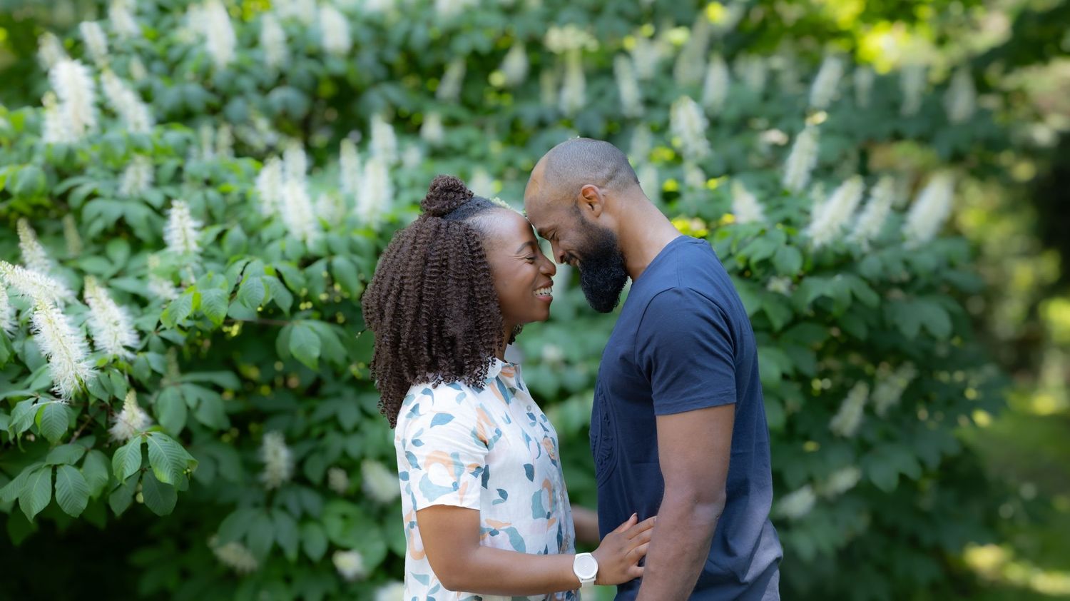 Romantic couple embracing outdoors against a backdrop of white flowering bushes.