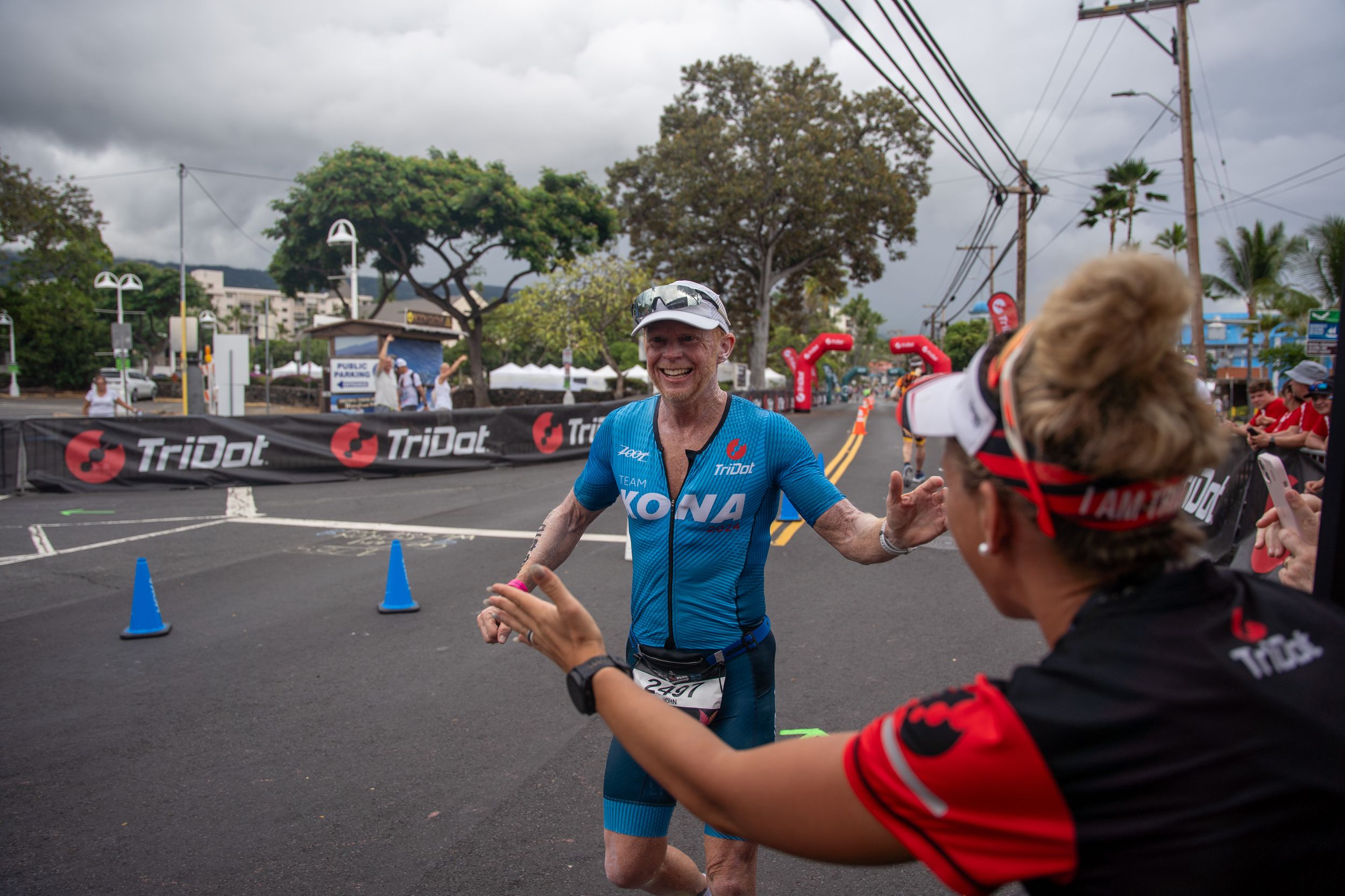 A triathlete in blue race gear receives hydration from a volunteer during a competition in Hawaii.