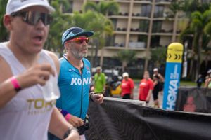 Athletes compete at a triathlon event with palm trees and race barriers visible in the background.