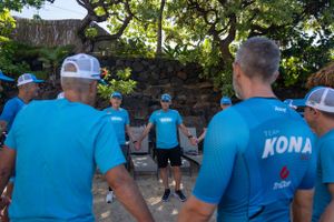 A group wearing matching blue t-shirts gathers outdoors near a stone wall during a team event.