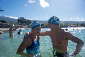 Swimmers wearing blue swim caps enjoy the turquoise waters at a scenic beach on a sunny day.