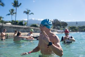 Swimmers enjoy the turquoise waters of a tropical pool with palm trees and mountains visible in the background.