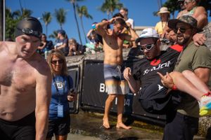 A crowd of spectators gathers outdoors at a beach event with palm trees visible in the background.