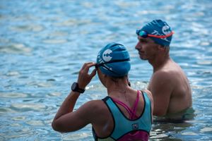 Two swimmers in blue swim caps stand in blue water during an outdoor swimming event.