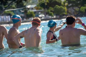 Swimmers wearing swim caps relax in a pool on a sunny day during an outdoor swimming event.