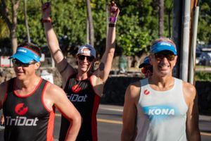 Three athletes in athletic gear celebrate during a triathlon event on a sunny day.
