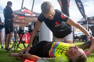 A massage therapist provides therapeutic treatment to an athlete lying on a table at an outdoor sporting event.