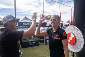 Two people in black shirts give each other a high five at an outdoor event with tents and a prize wheel visible.