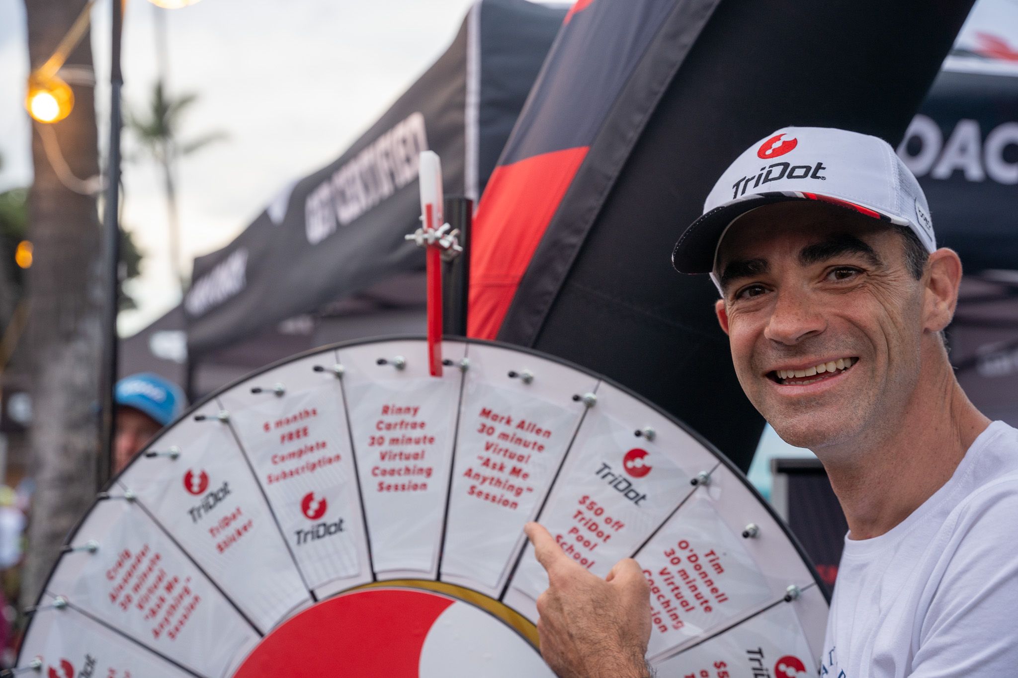 A participant holds up a large promotional prize wheel with red and white sections at an outdoor sporting event.