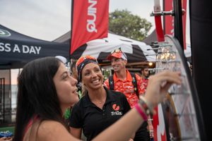 People enjoying drinks and conversation at an outdoor event with red banners and tents visible in the background.