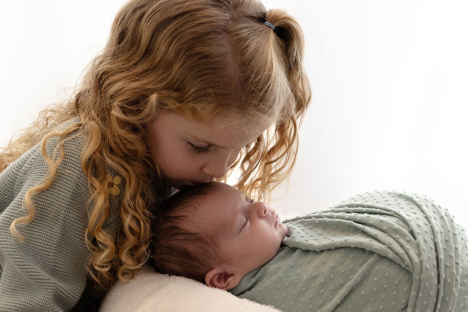 A tender moment of a child gently kissing someone who appears to be resting on a neutral background.