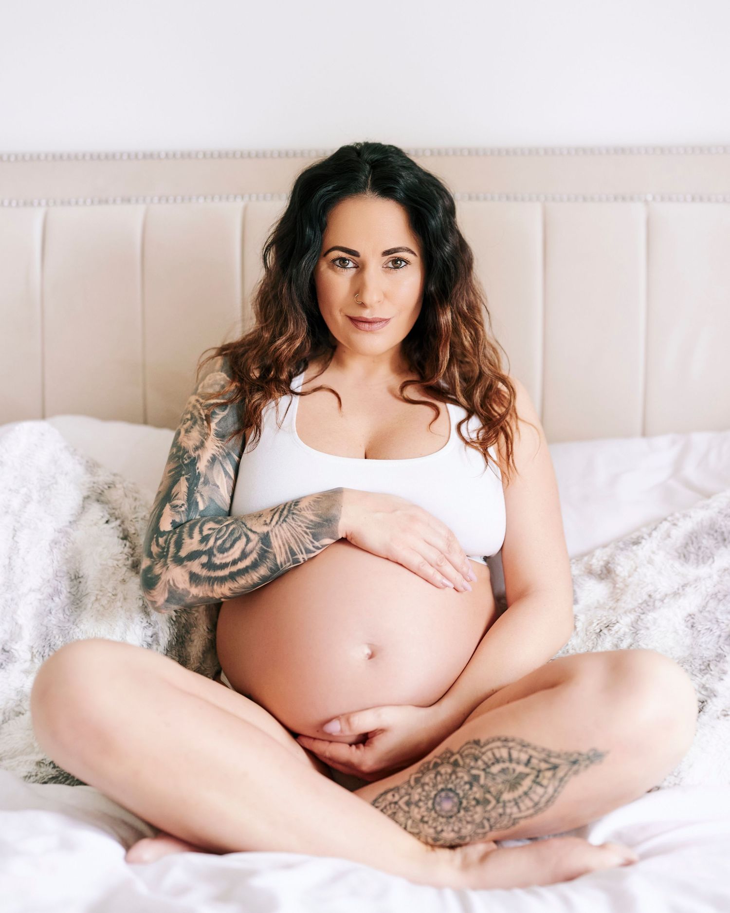 Pregnant woman in Gloucestershire having a maternity photoshoot. She is sitting on a bed hugging her baby to be.