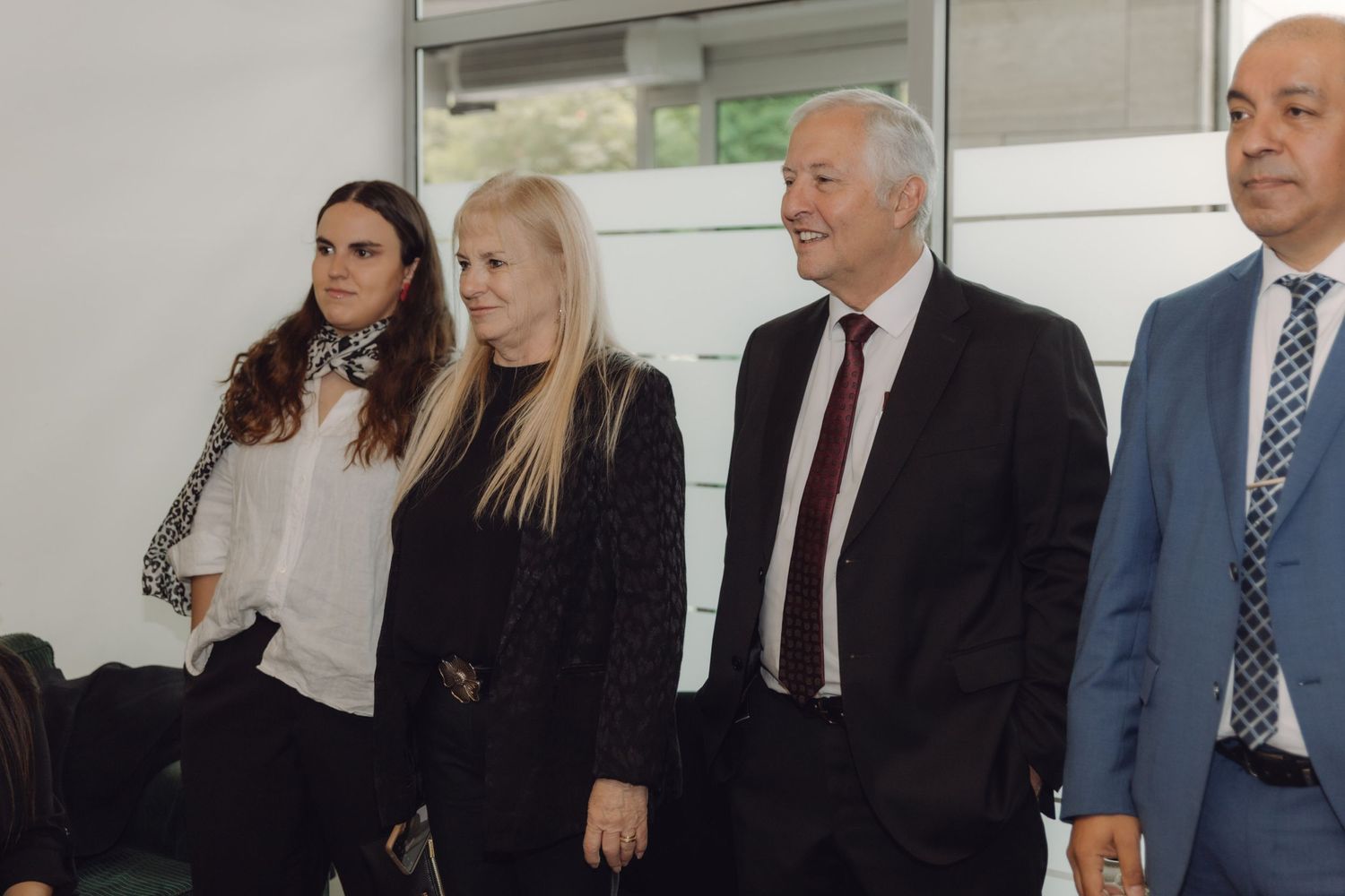Four professionally dressed people standing together indoors at a formal business or official event.