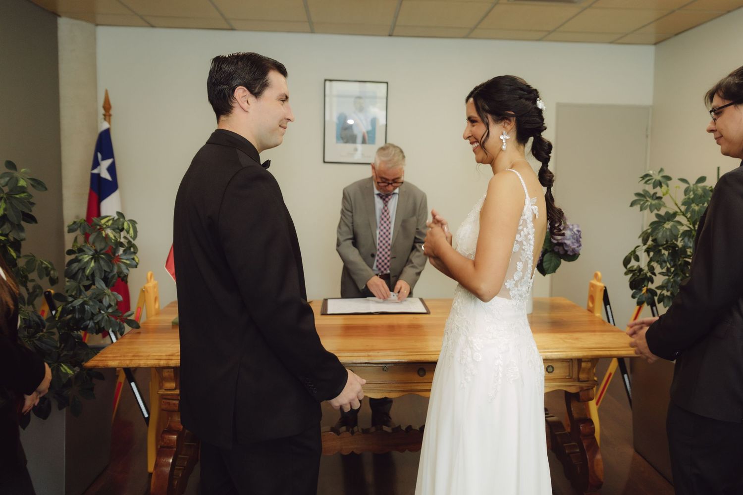 Smiling bride and groom exchange vows before officiant signing documents at wedding ceremony.