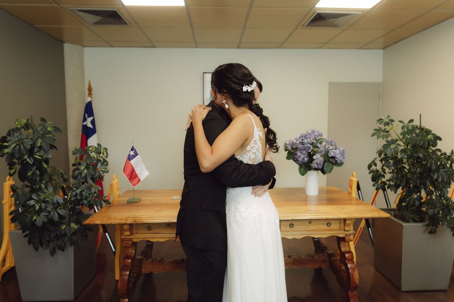 Bride and groom share tender embrace holding bouquet after civil wedding ceremony.