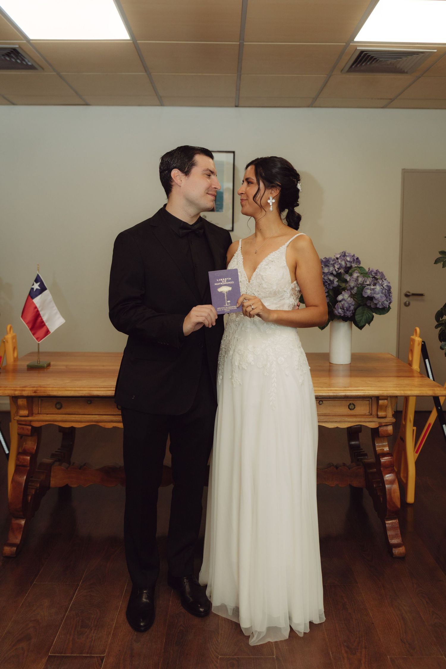 Newlywed couple gazes at each other holding marriage booklet at civil wedding ceremony.