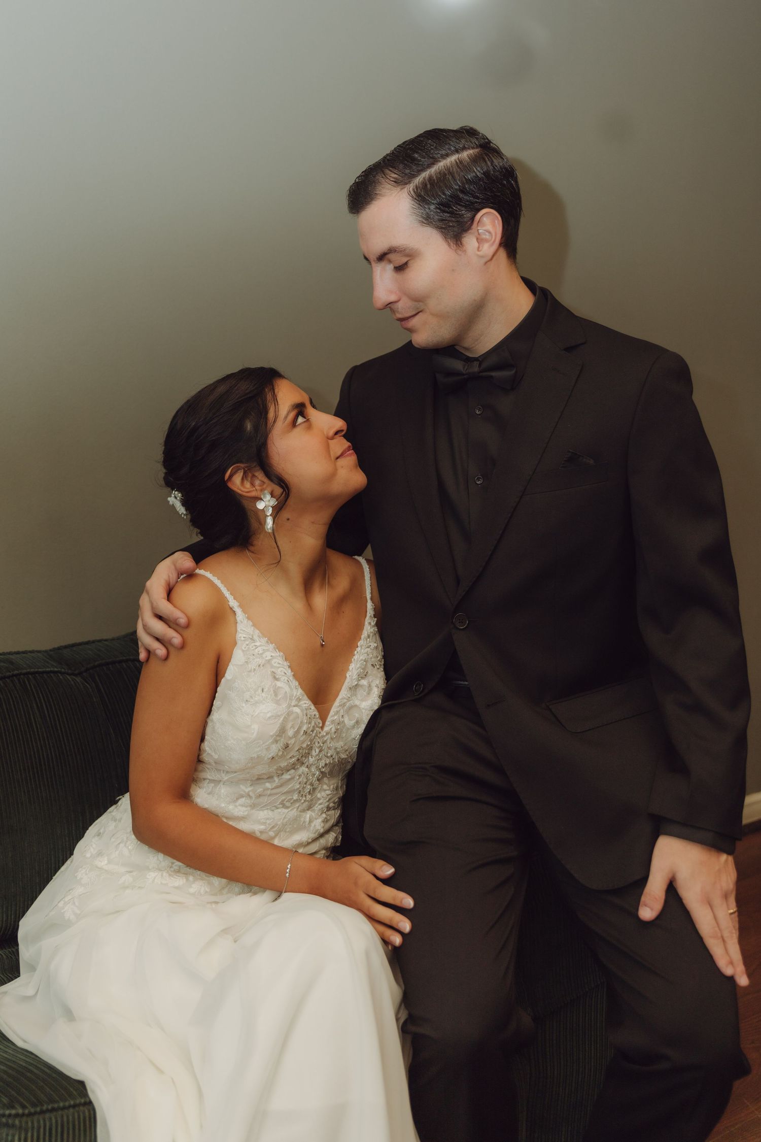 Bride and groom sitting together on a couch, sharing a tender moment in wedding attire.