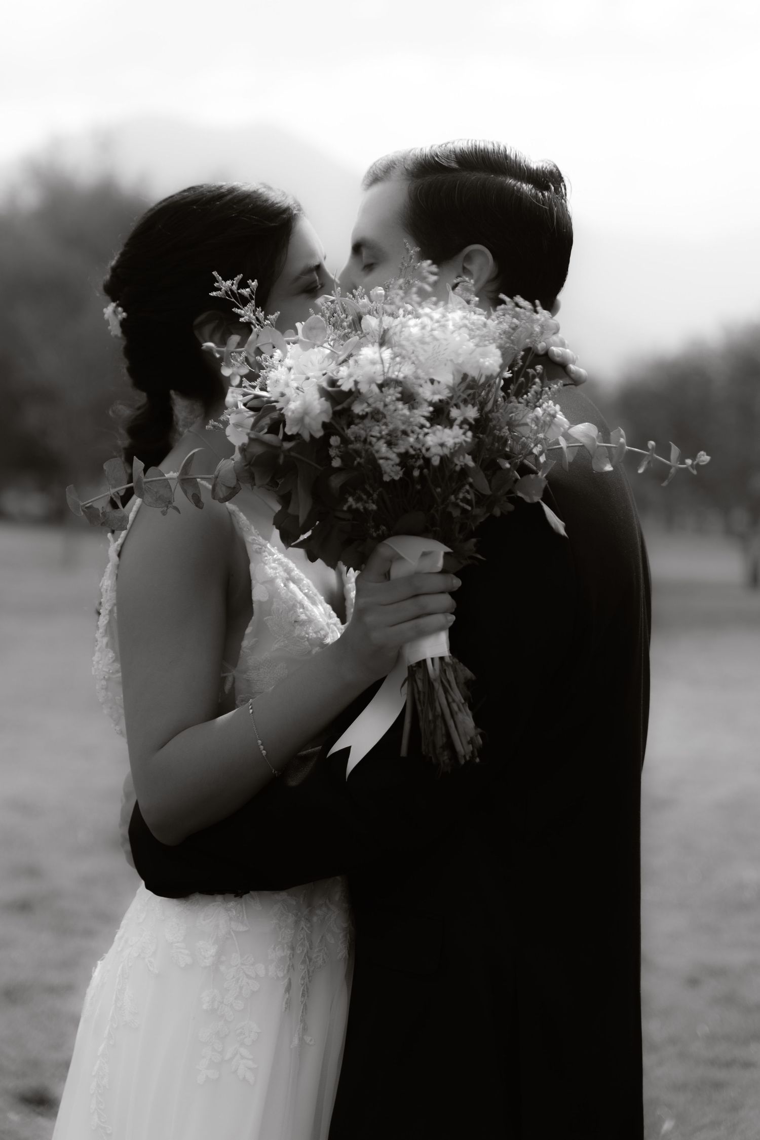 Black and white photo of bride and groom kissing behind a beautiful wedding flower bouquet.