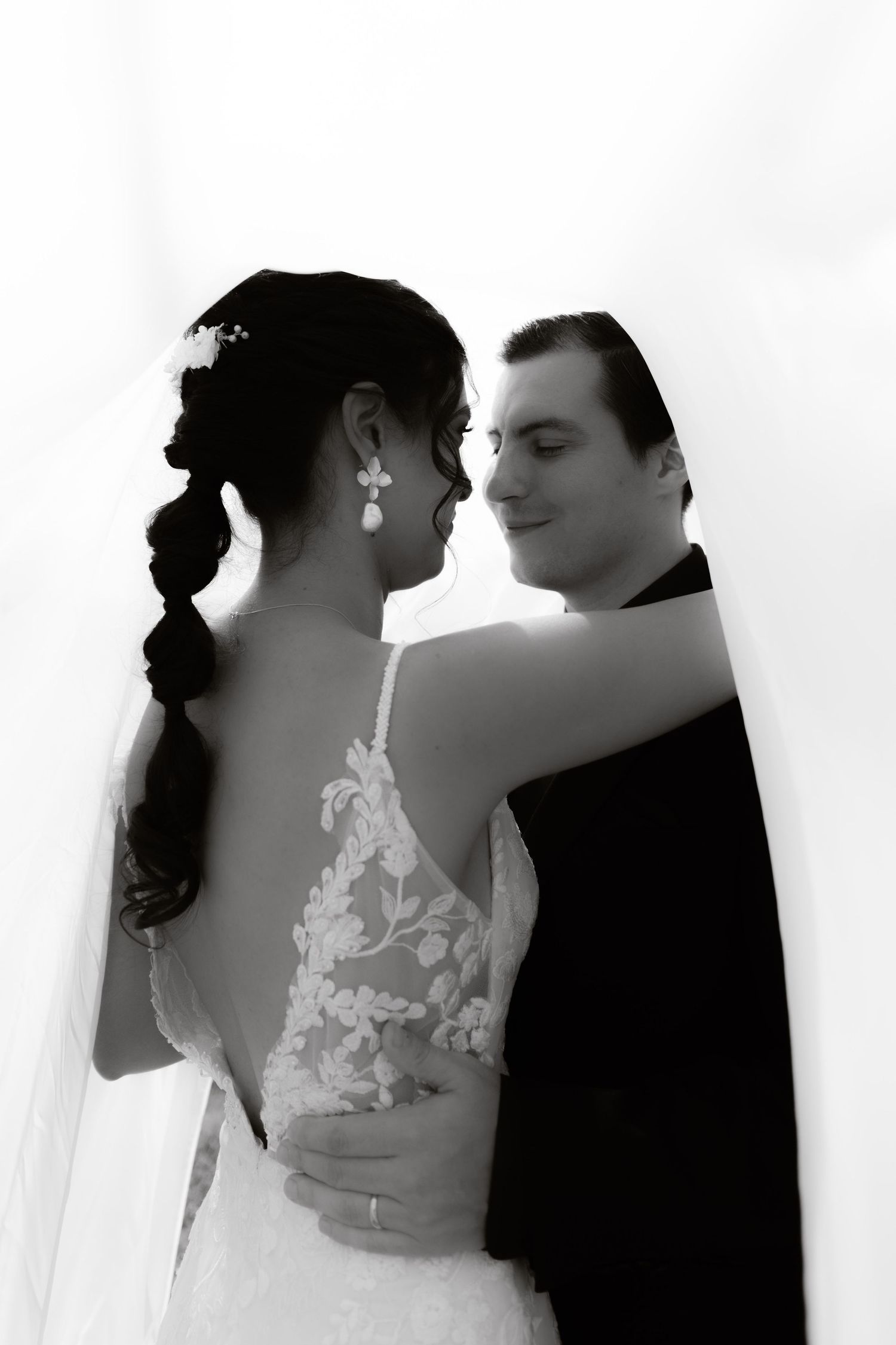 Black and white portrait of bride and groom embracing, showcasing the lace back of bridal gown.