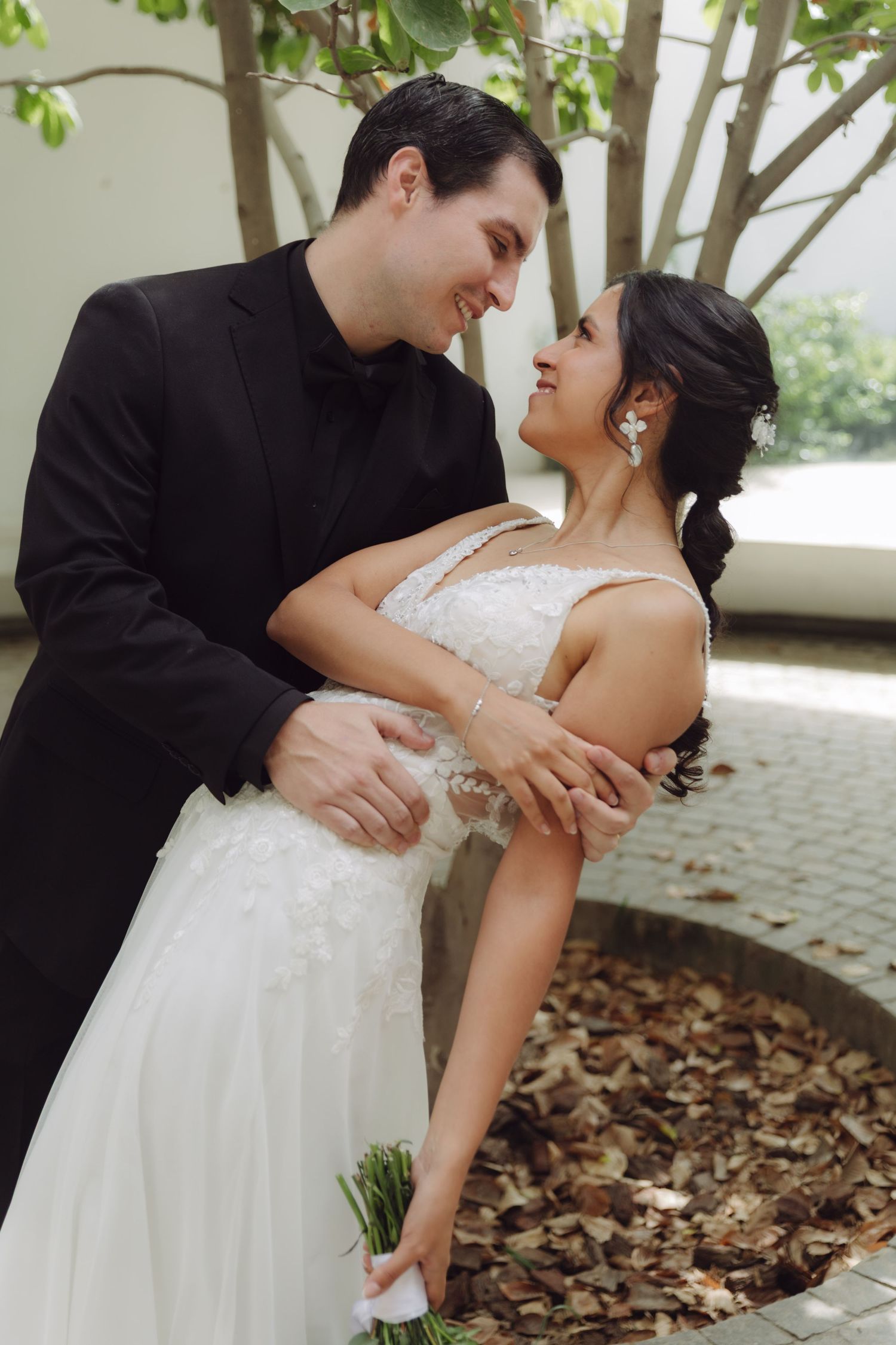Groom in black tuxedo dipping bride in white lace wedding gown, smiling at each other.