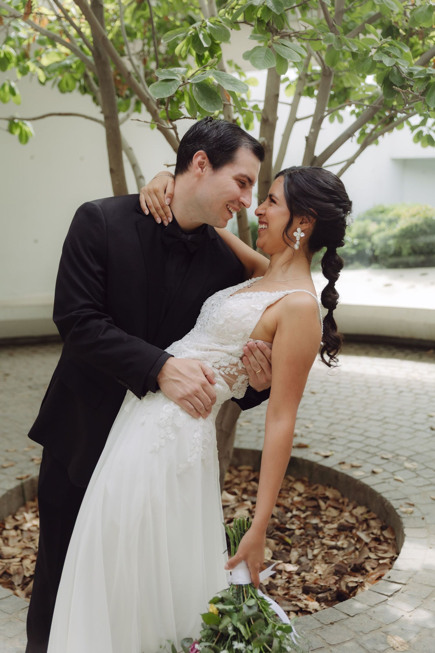 Wedding couple gazing lovingly at each other near a circular garden bed with fallen leaves.