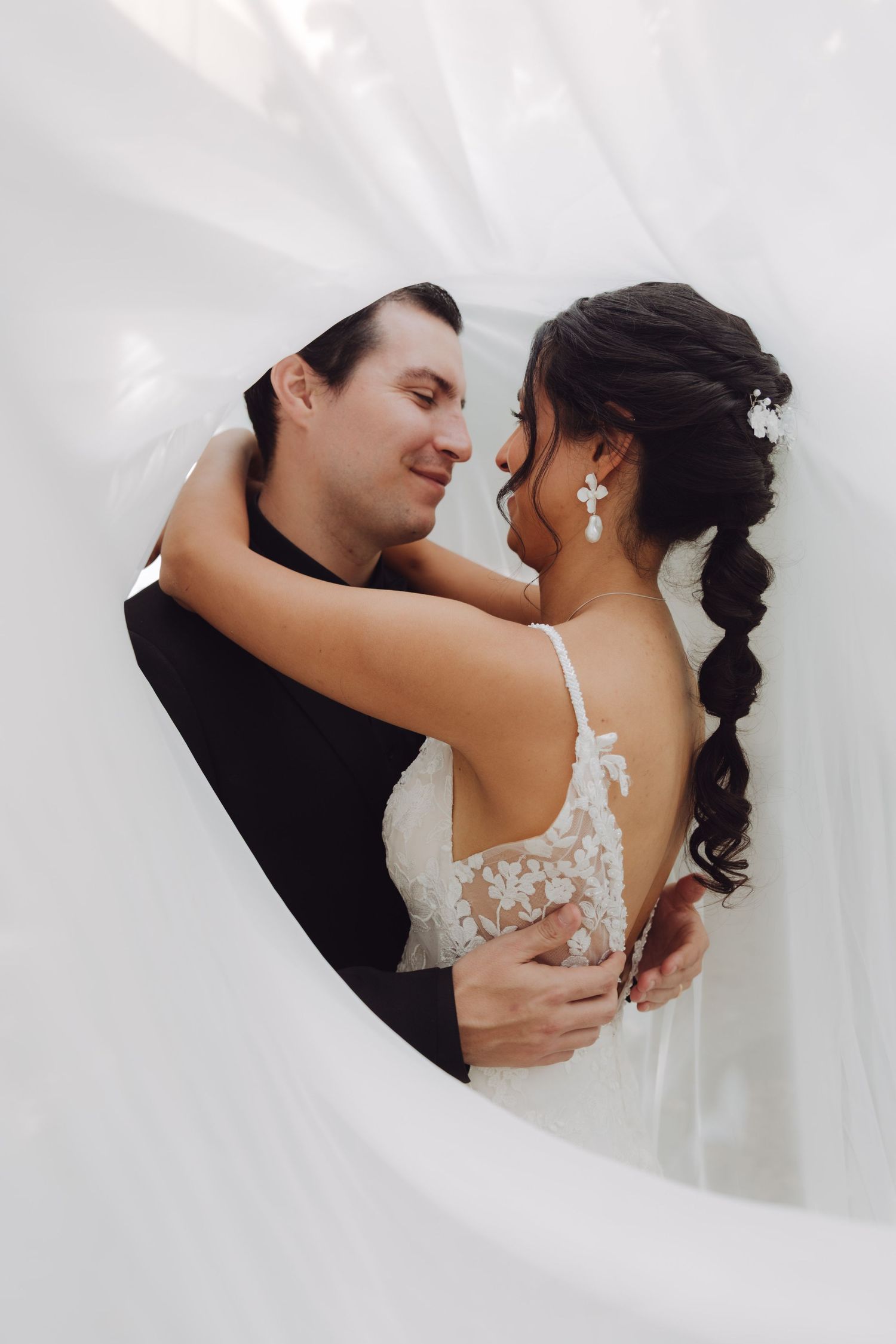 Bride and groom embracing romantically framed by a billowing white veil in a heart shape.