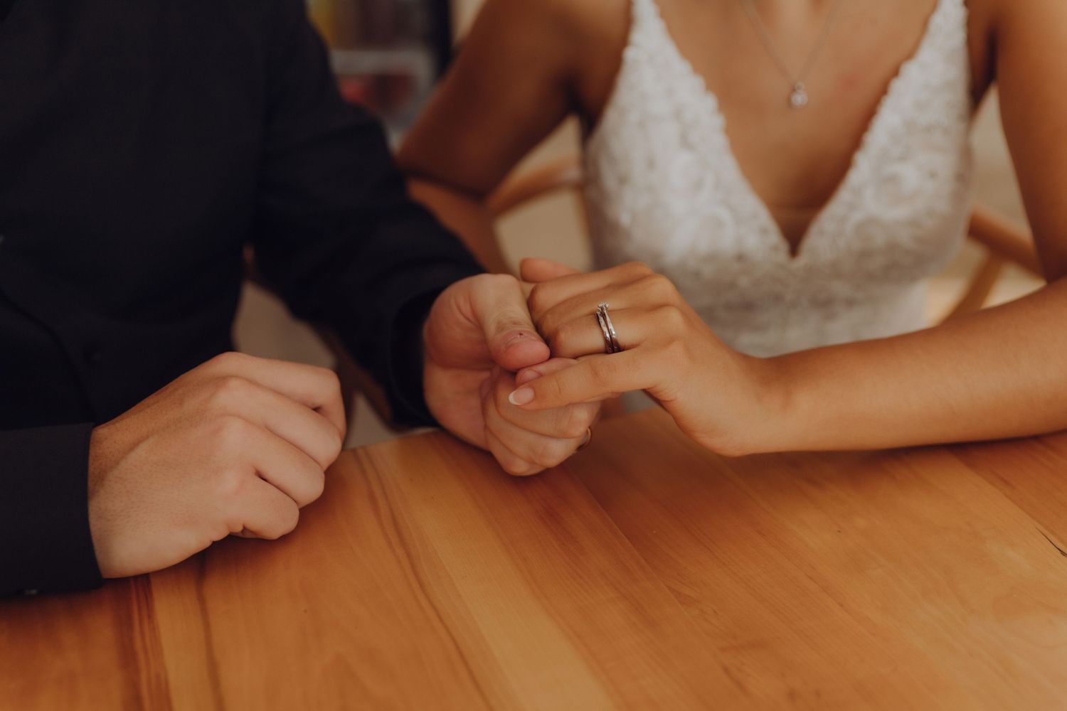 Newlyweds hold hands on wooden table showing wedding rings close-up.