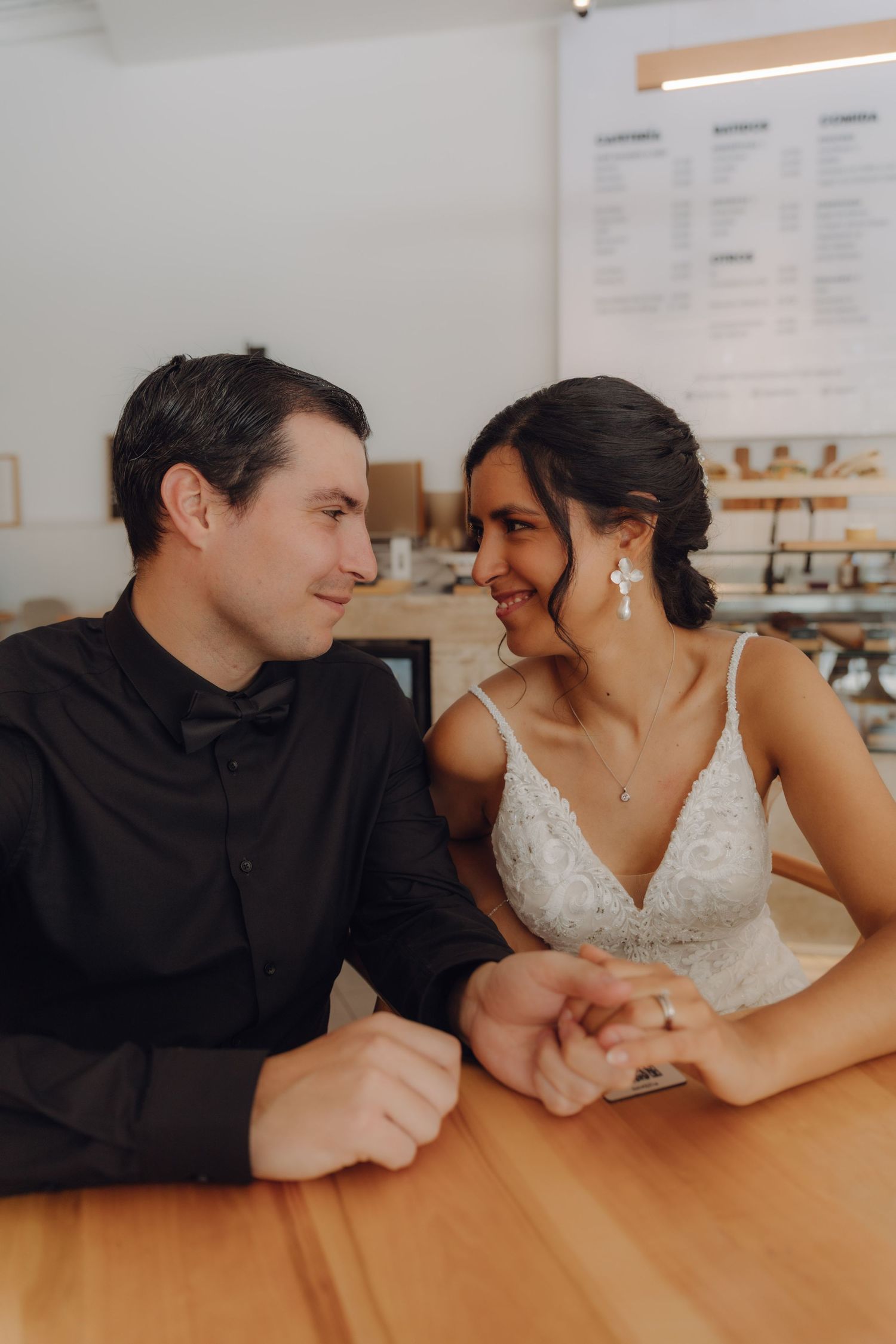 Bride and groom holding hands and smiling at each other while seated at a wooden counter.