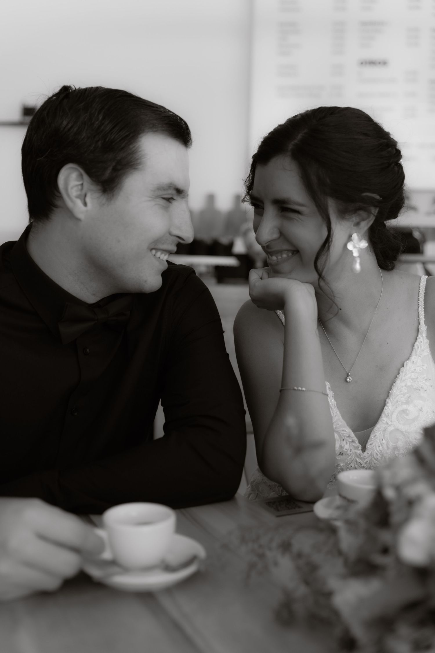 Bride and groom share a joyful moment over coffee in black and white photo.