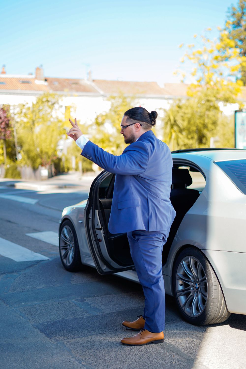 Man in blue suit gesturing while standing next to luxury car door.