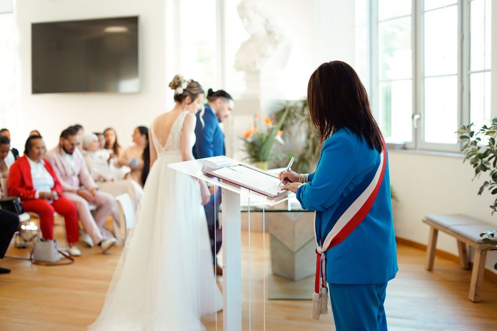 Wedding ceremony taking place indoors with official in blue conducting the proceedings.