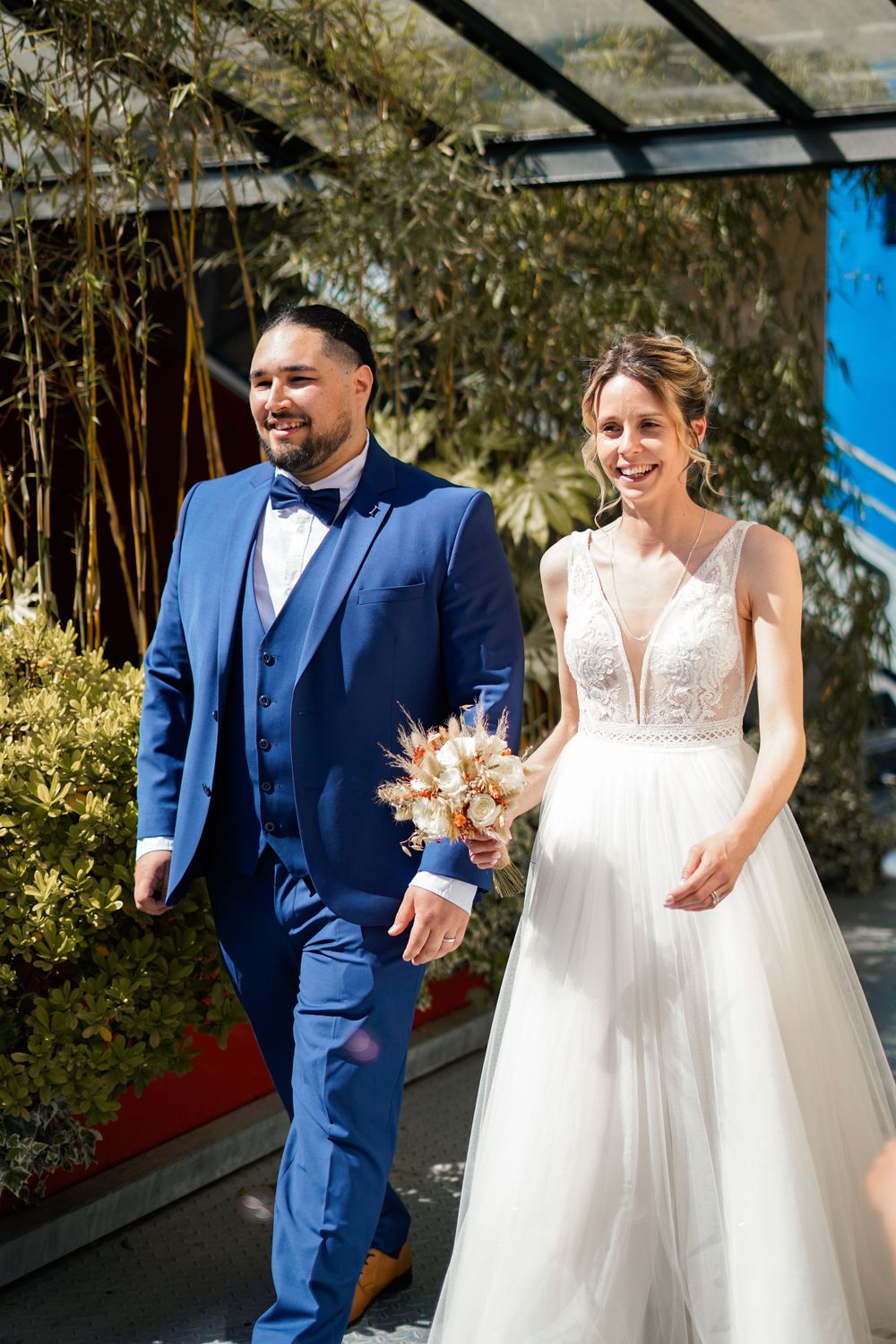 Newlyweds walking together outdoors, with bride in white dress and groom in navy suit.