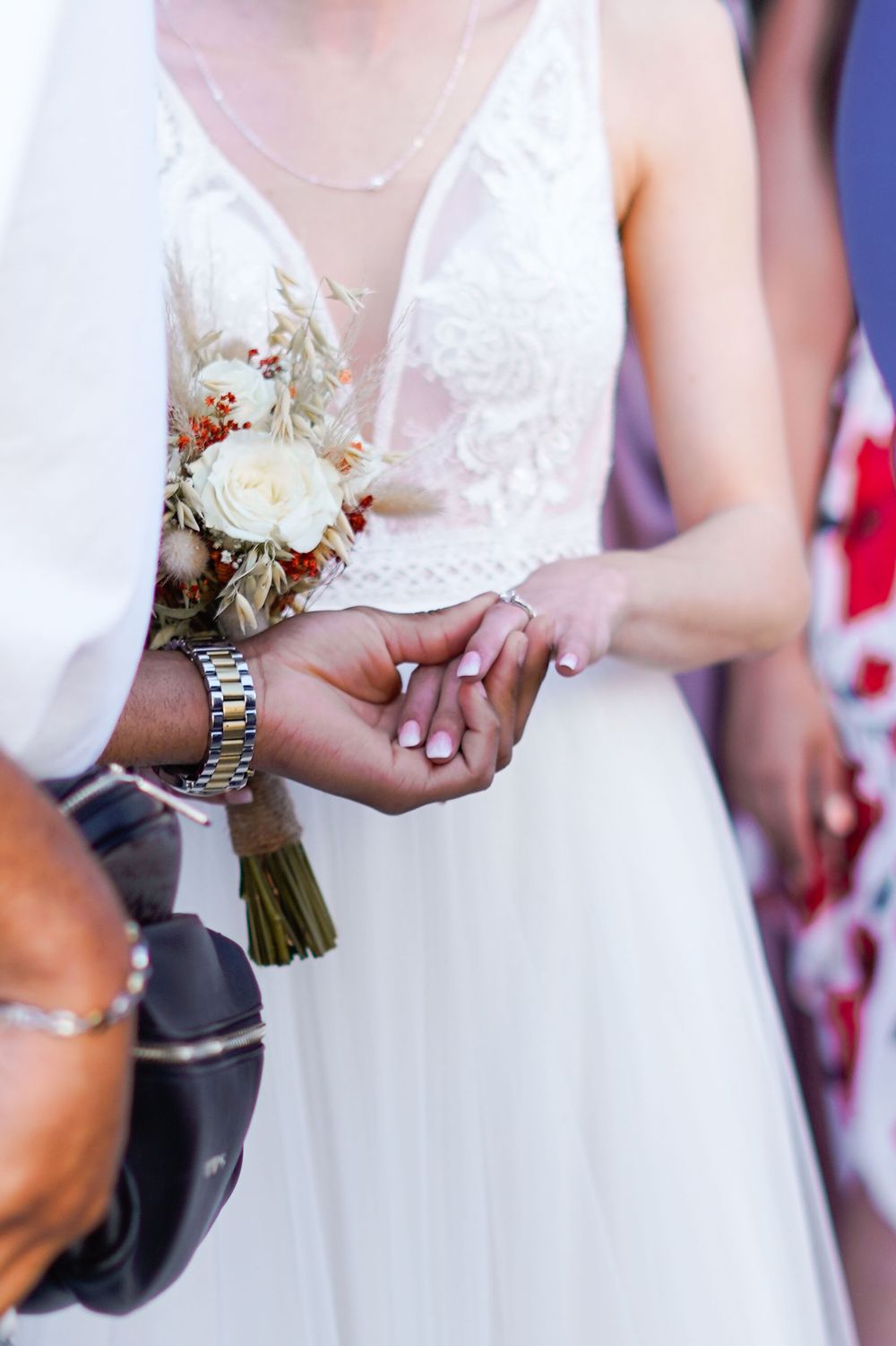 Close-up of hands holding a delicate white and peach wedding bouquet during ceremony.