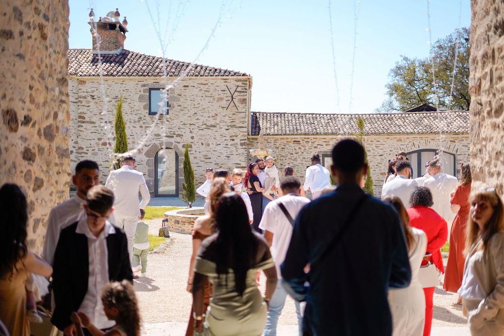 Wedding guests gathered in a sunny stone courtyard.